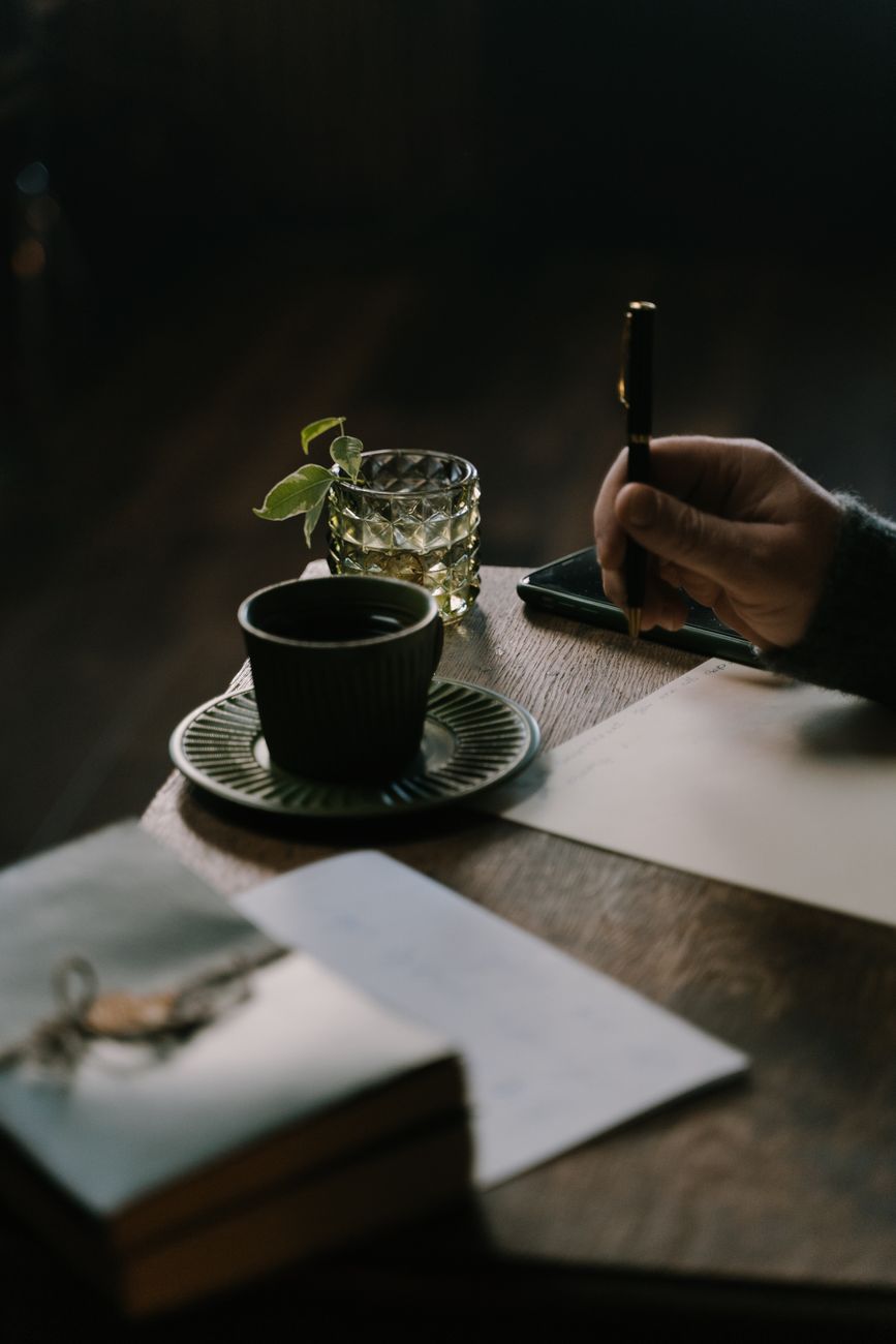 A consultation table just after the conversation: an open notepad with handwritten figures beside a coffee mug on a wooden table, late-morning light raking through blinds, shallow depth of field.